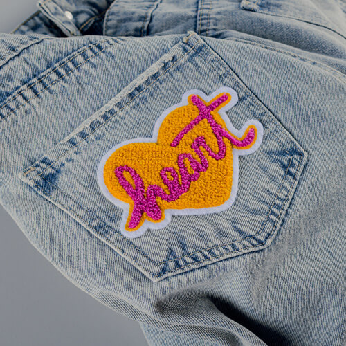 Chenille Heart Shaped Patch with the word heart in the center applied to jeans